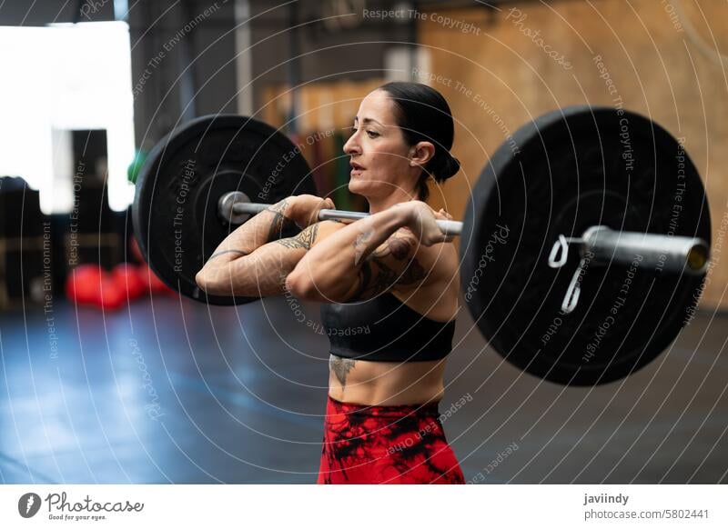 Starke, konzentrierte Frau hebt Gewichte in einem Fitnessstudio stark reif Heben Cross-Training Übung Stärke Gesunder Lebensstil anstrengen Tattoo Ermächtigung