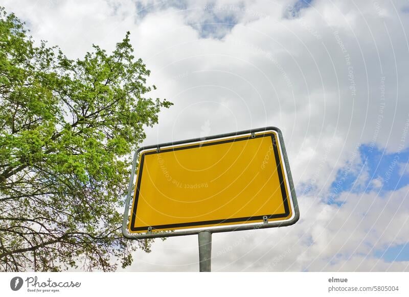 leeres Ortseingangsschild aus der Froschperspektive, ein Laubbaum und Wolkenhimmel Ortsschild Hinweisschild Schilder & Markierungen Textfreiraum beschriftbar