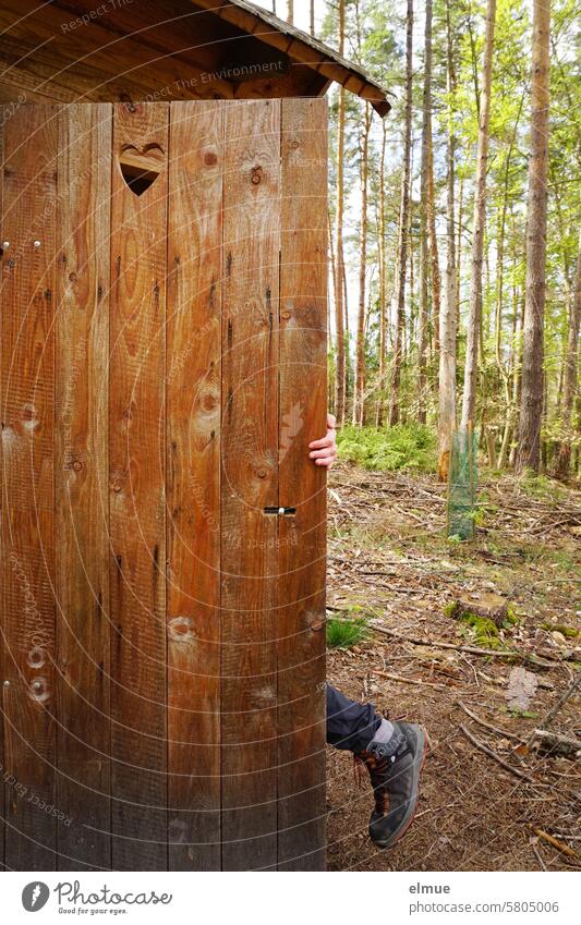 Hand und Bein einer Person, die im Wald in einem Plumpsklo mit Herzchen in der Tür verschwindet Trockenklo Bioklo Biotoilette Gartenklo Gartentoilette Waldklo