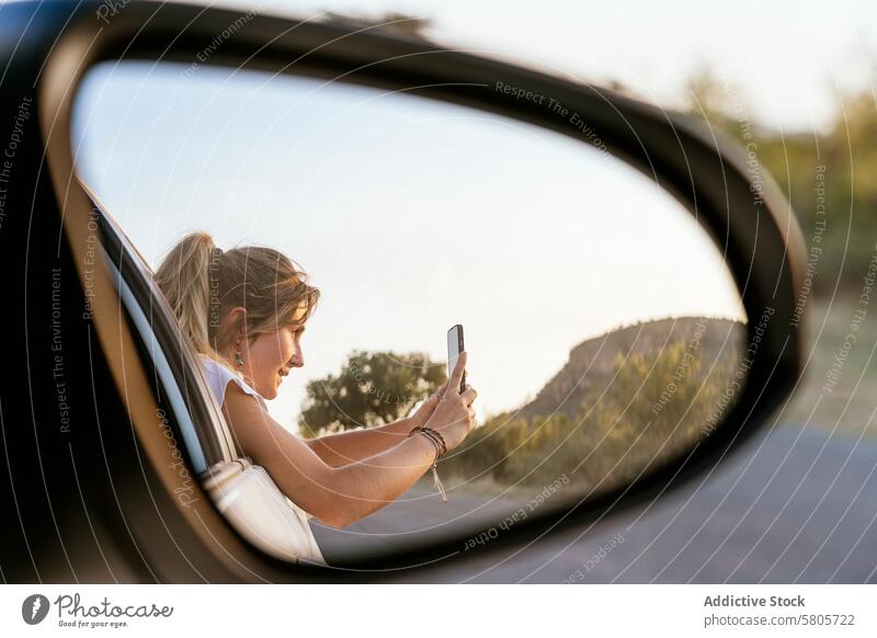 Frau, die die Landschaft mit ihrem Handy durch den Autospiegel erfasst Smartphone PKW Seitenspiegel Reflexion & Spiegelung im Freien malerisch Foto erfassend