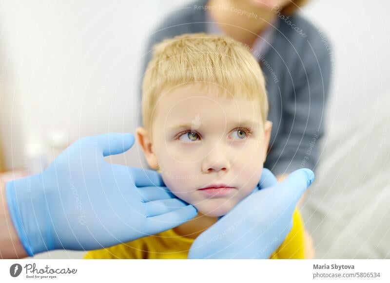 Ein niedlicher kleiner Junge und seine Mutter haben einen Termin bei einem Kinderarzt. Der HNO-Arzt untersucht die Lymphknoten eines kleinen Patienten.