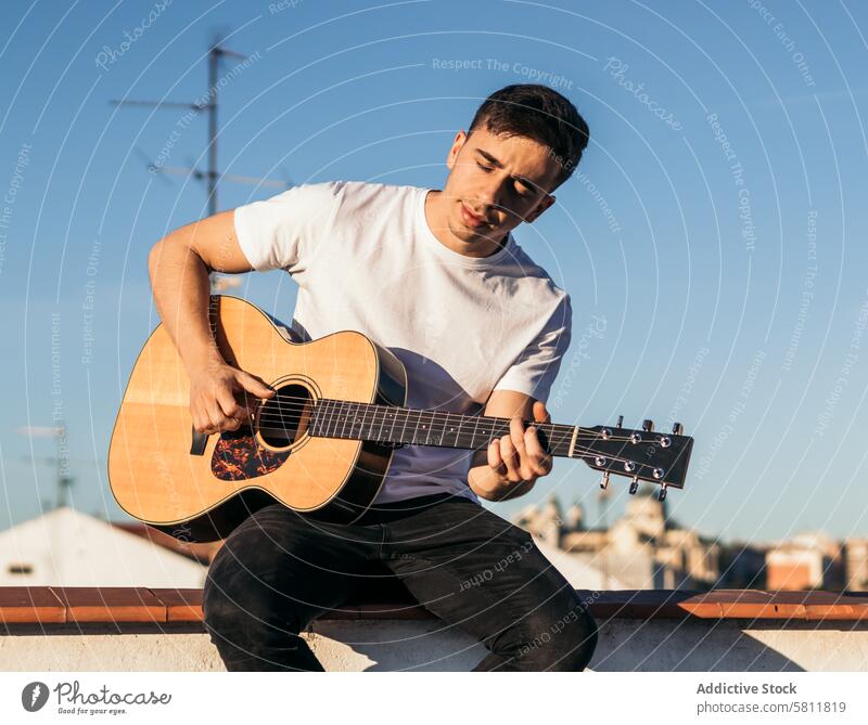 Junger Mann sitzt auf einem Dach und spielt Akustikgitarre Gitarre Musiker Gitarrenspieler akustisch jung Sitzen männlich Person Instrument Spieler Musical