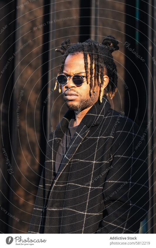 Stilvoller schwarzer Mann mit Dreadlocks im Dutt Streetstyle cool Rastalocken urban modern Mantel Sonnenbrille Frisur Brötchen Stirnrunzeln informell trendy