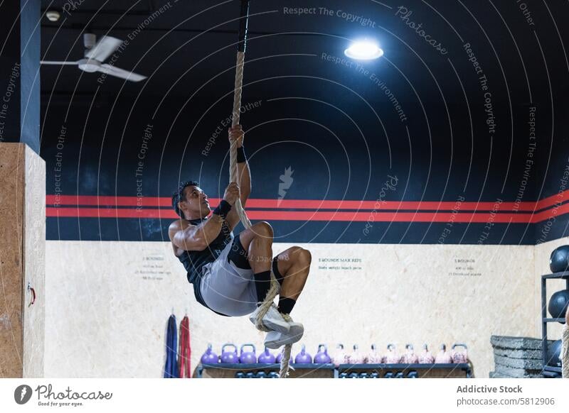 Starker Sportler beim Klettern am Seil Athlet Training Fitnessstudio Übung üben sportlich Mann Sportkleidung Sportbekleidung Wellness Hobby muskulös physisch