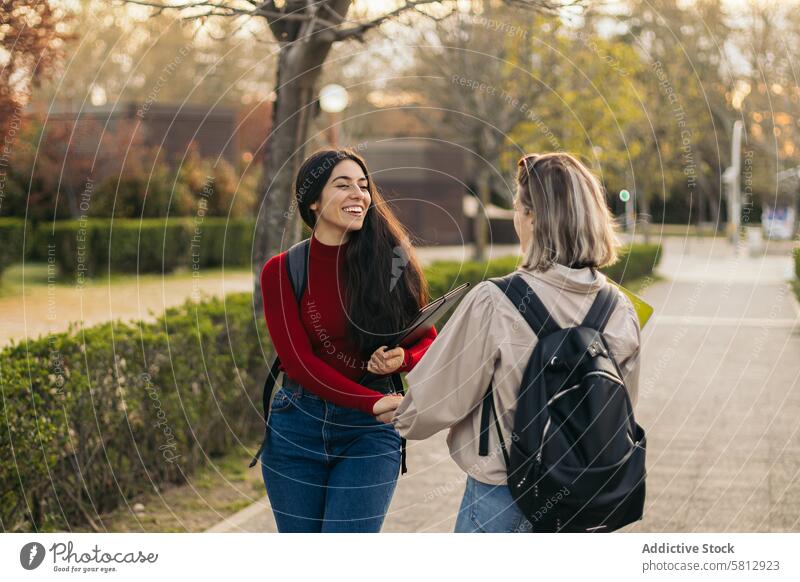 Rückenansicht von zwei Studentinnen im Gespräch und lachend Mädchen Frau Glück Seite Zusammensein Freundschaft sprechend Freunde Freundin jung Menschen Schüler