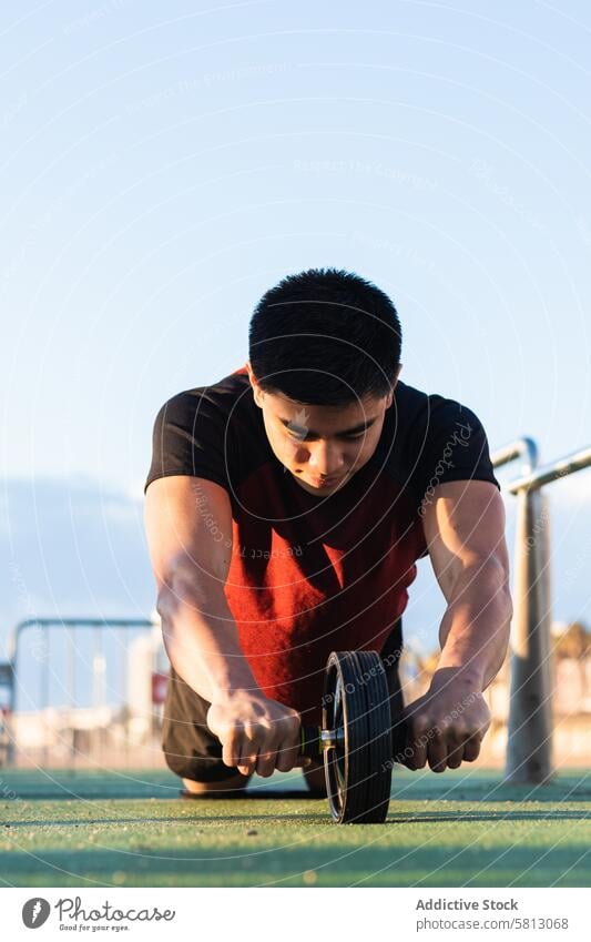 Muskulöser Mann bei einer Bauchmuskel-Rollout-Übung Sportler ab Rad Rolle Bauchmuskeln Training Athlet Fitness intensiv muskulös Kerngehäuse Sportpark physisch