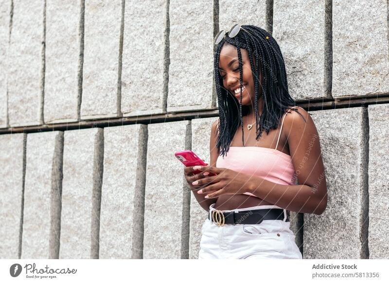 Porträt einer schwarzen jungen Frau, die sich mit ihrem Smartphone in der Stadt vergnügt Afroamerikaner Sommer Jugend Mitteilung Freude lachen Fröhlichkeit