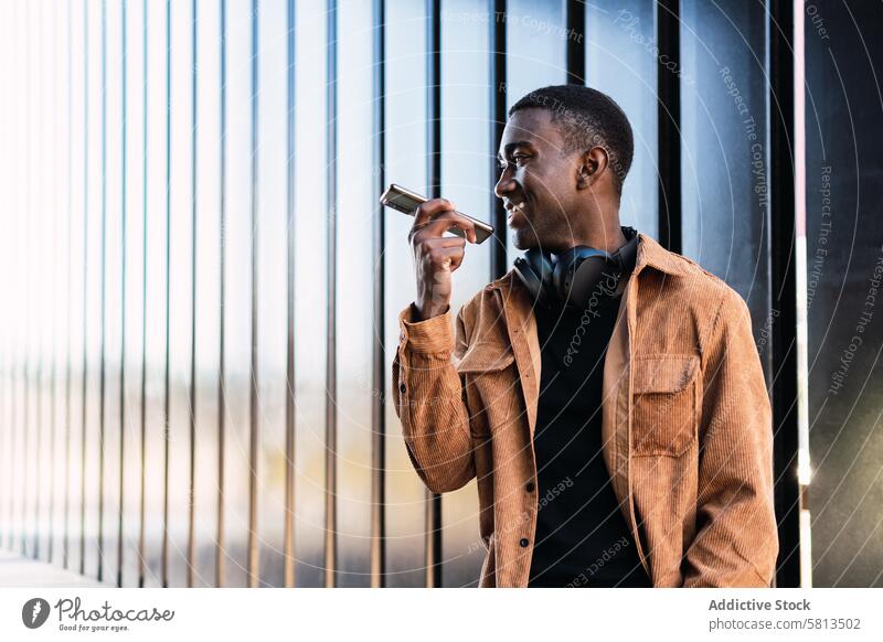 Schwarzer Mann mit Kopfhörern, der eine Sprachnachricht aufnimmt Smartphone Stimme Nachricht Audio meloman Wand Straße Aufzeichnen Großstadt benutzend Anschluss