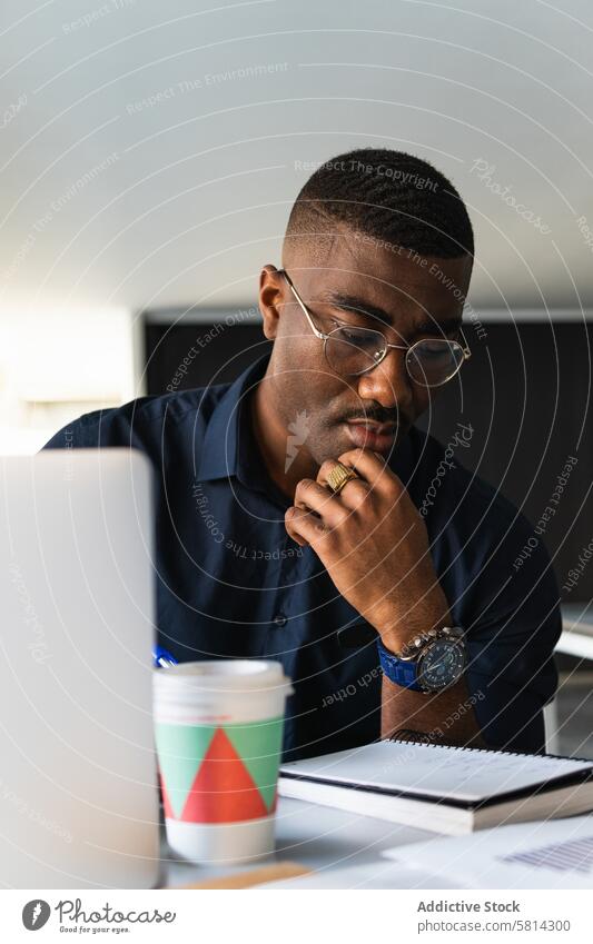 Afroamerikanischer Mann, der in der Nähe eines Laptops im Büro in einen Notizblock schreibt zur Kenntnis nehmen Notebook Netbook Tisch Schriftstück