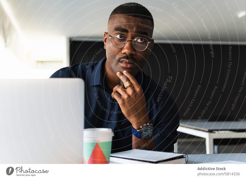 Afroamerikanischer Mann, der in der Nähe eines Laptops im Büro in einen Notizblock schreibt zur Kenntnis nehmen Notebook Netbook Tisch Schriftstück