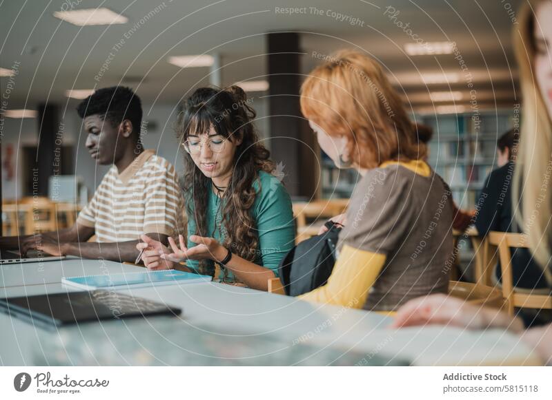 Junge heterogene Gruppenmitglieder unterhalten sich in der Bibliothek während der Prüfungsvorbereitung Schüler reden Menschen Bildung diskutieren Zusammensein