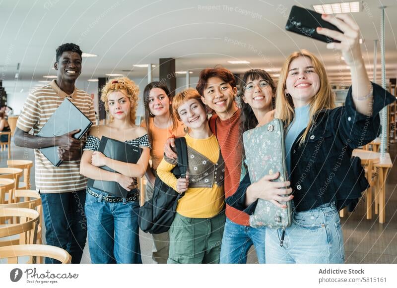 Gemischtrassige Klassenkameraden machen ein Selfie in der Bibliothek Schüler Universität Smartphone Zusammensein Lächeln Umarmung Freund Menschengruppe