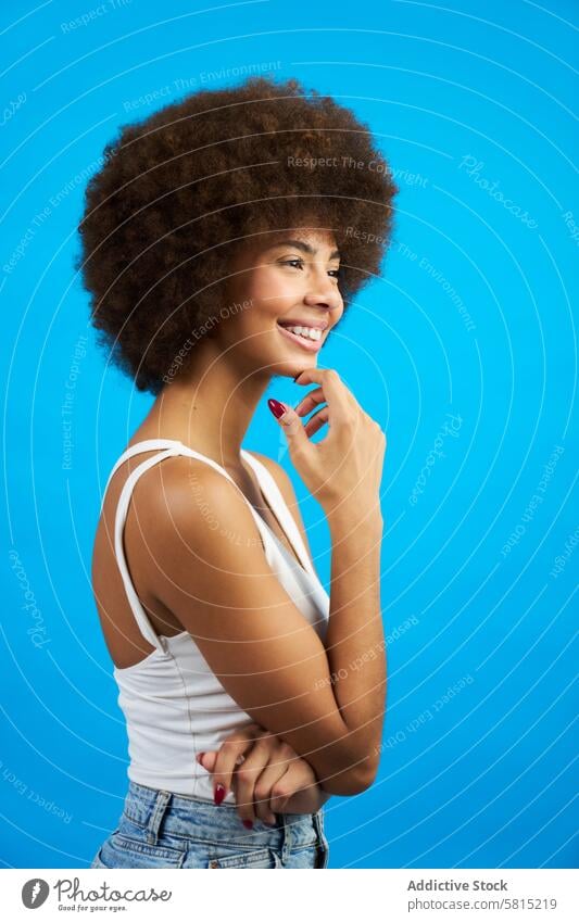 latina frau mit afro haar im profil mit hand auf kinn lächelnd studio foto mit blauem hintergrund lateinamerikanisch Frau Afro-Look Behaarung Hintergrund