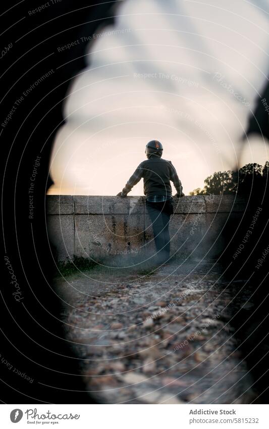 Anonyme Person mit Helm und Blick auf den Horizont in der Abenddämmerung Schutzhelm Mann Starrer Blick Dämmerung Kontemplation Abenteuer Wand alt Stehen einzeln