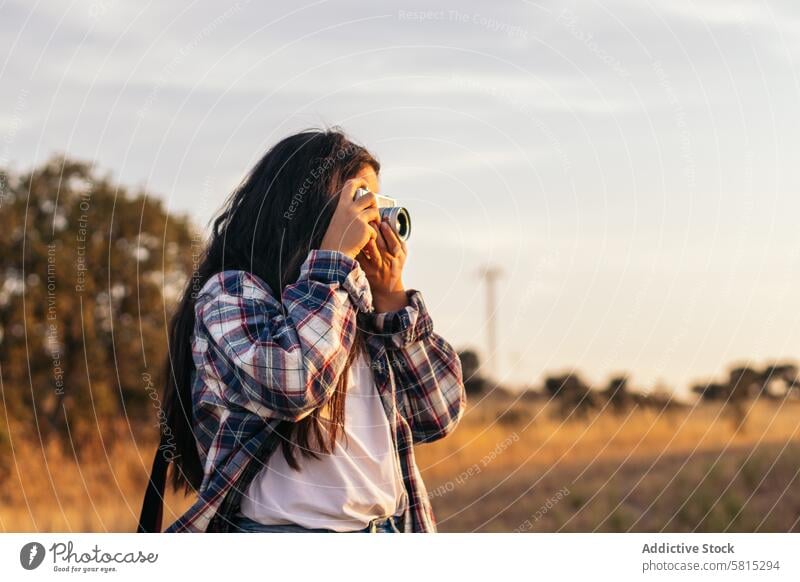 Junge Frau, die mit einer analogen Kamera im Feld bei Sonnenuntergang fotografiert Foto Lifestyle jung Mädchen Fotografie altehrwürdig Fotokamera retro reisen