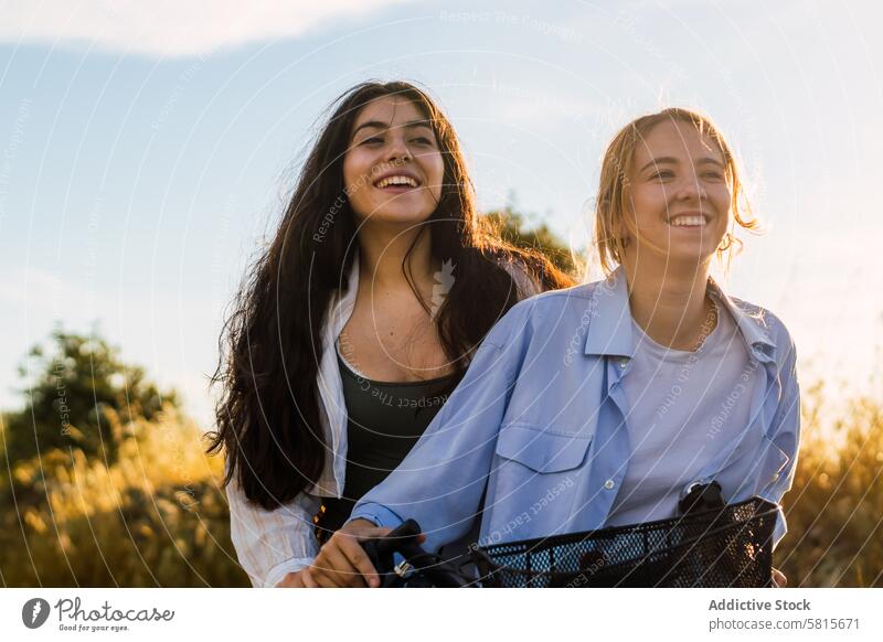 zwei junge Frauen auf einem Fahrrad in einem Feld bei Sonnenuntergang Lifestyle Sommer Natur Glück Himmel Mädchen Freizeit Menschen Paar Zusammensein