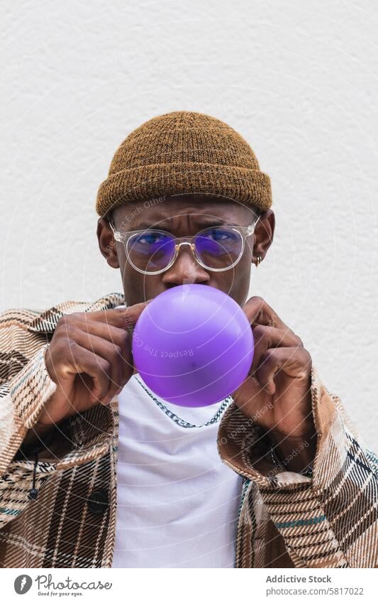 Trendy ethnischen Mann bläst Ballon Schlag Luftballon Stil urban Straße lässig jung Großstadt modern männlich schwarz Afroamerikaner Hut Brille Mode Outfit