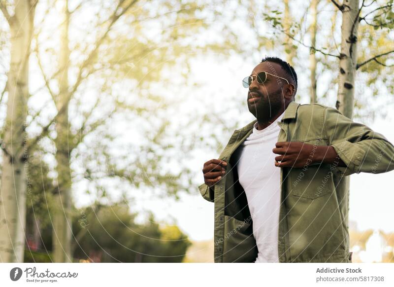 Stilvoller afroamerikanischer junger Mann mit Sonnenbrille beim Spaziergang in einem Park attraktiv gutaussehend Amerikaner Afrikanisch Glück Person männlich