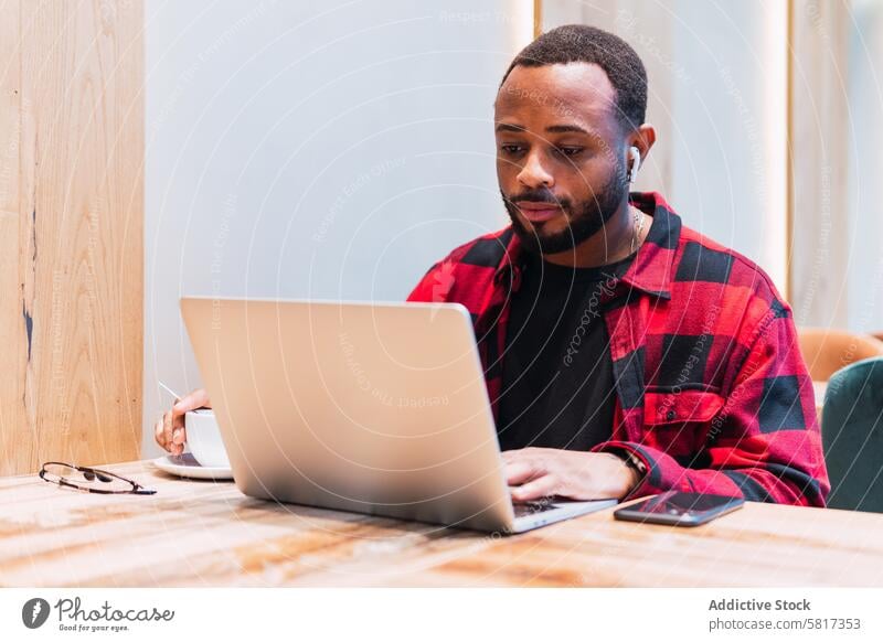 Schwarzer Mann arbeitet in einem Café an einem Laptop Kopfhörer benutzend online Internet Browsen freiberuflich Arbeit männlich schwarz Afroamerikaner Netbook