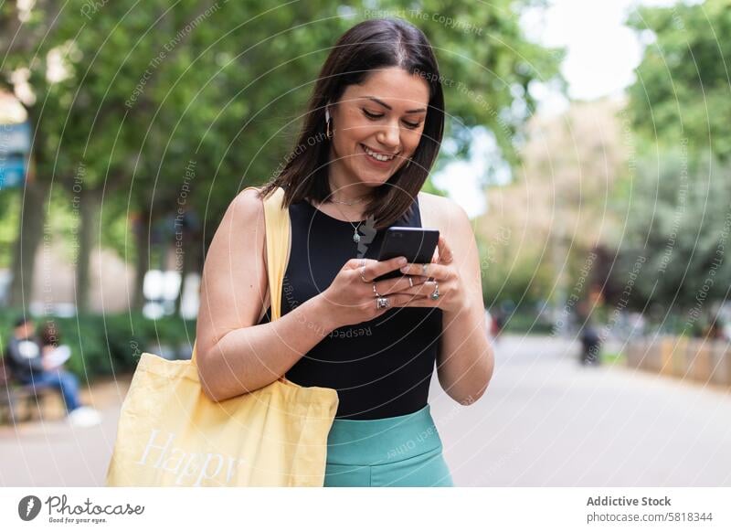 Lächelnde Frau, die in der Stadt auf ihrem Smartphone Nachrichten schreibt benutzend Talkrunde online soziale Netzwerke Mobile Browsen Telefon Straße Surfen