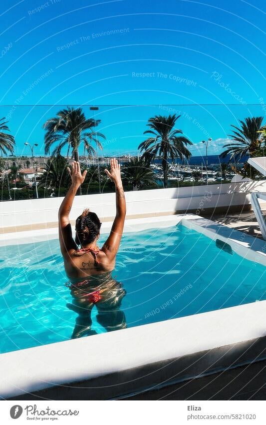 Frau mit erhobenen Armen im Sommerurlaub im Pool Urlaub baden Meerblick Palmen Bikini braungebrannt Lifestyle Wasser Schwimmen & Baden blau