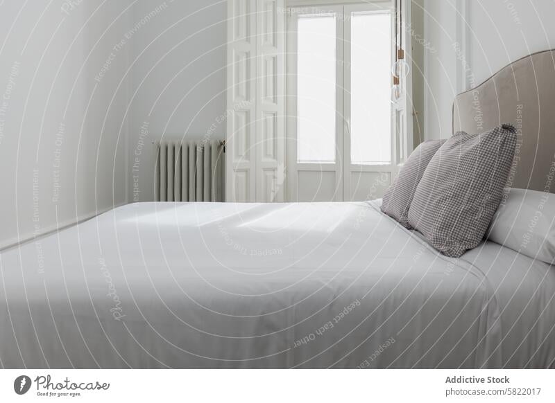 Gelassenes Schlafzimmer mit natürlichem Licht und klassischem Design Bett Kopfkissen minimalistisch weiß natürliches Licht Fenster gemütlich Komfort Einfachheit