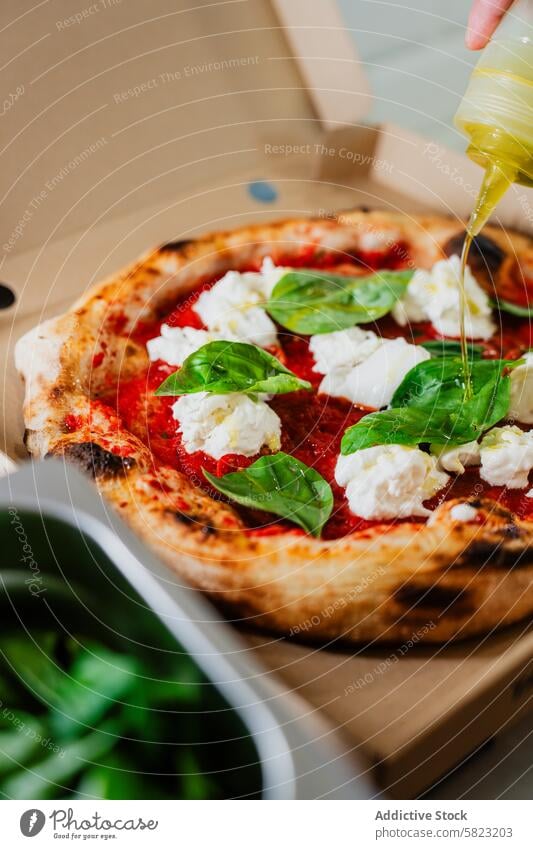 Beträufeln einer frischen Pizza Margherita mit Olivenöl in einer Pizzeria Nieselregen margherita Mozzarella Basilikum gebacken Karton Kasten Takeout Servieren