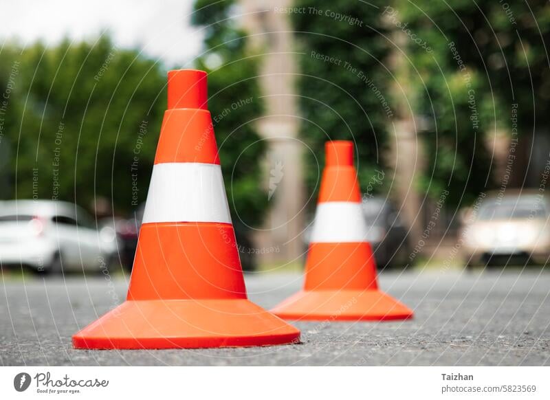 Leuchtend rote orangefarbene Verkehrskegel stehen in einer Reihe auf einem Asphalt in der Stadt. Niedriger Blickwinkel. Nahaufnahme Hintergrund Begrenzung PKW