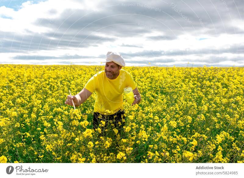 Mann im gelben Hemd malt Blumen in einem blühenden Feld Landwirt Raps Ackerbau wolkig Himmel männlich Bepflanzung inspizierend pulsierend Natur im Freien