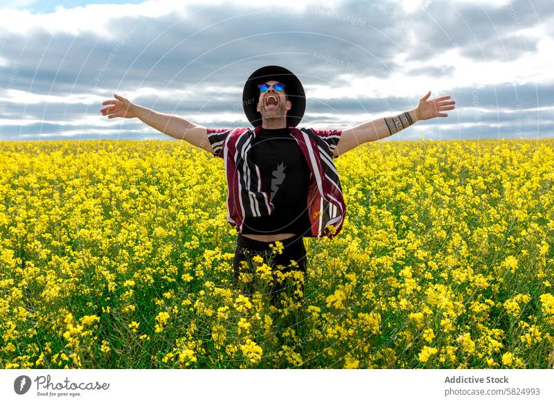 Feiernder Mann in einem leuchtend gelben Rapsfeld Feld Blume Freude Freiheit Fröhlichkeit ausgestreckte Arme bewölkter Himmel Natur im Freien Frühling