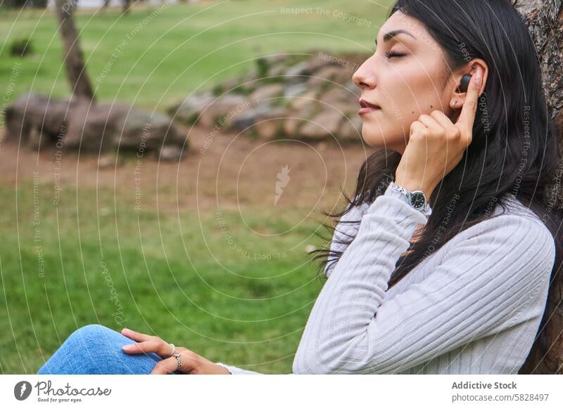 Gelassene Frau, die einen friedlichen Moment in einem grünen Park genießt entspannend ruhig Gelassenheit Baum Natur Freizeit meditierend im Freien Wellness