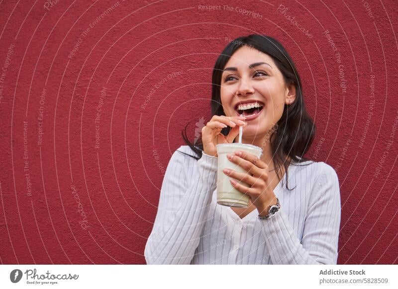 Fröhliche junge Frau genießt ein Getränk im Freien heiter Lachen trinken Erholung Fröhlichkeit Freizeit rote Wand Hintergrund pulsierend Freizeitkleidung Freude