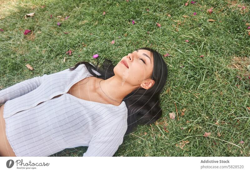 Friedliche junge Frau auf Gras in einem Park liegend entspannend Natur friedlich Ruhe Gelassenheit Freizeit im Freien grün Blütenblätter Windstille Lifestyle