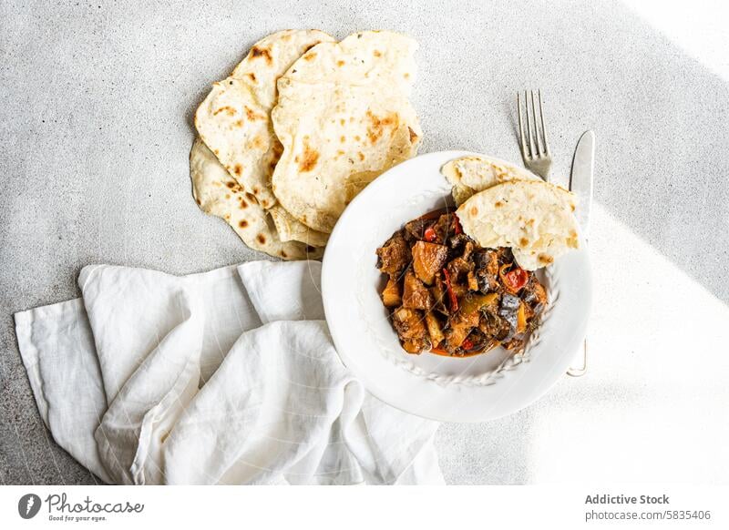 Hausgemachter Gemüseeintopf und Fladenbrot auf weißer Unterlage schmoren selbstgemacht Aubergine Tomate Kartoffel Paprika Zwiebel Knoblauch Basilikum