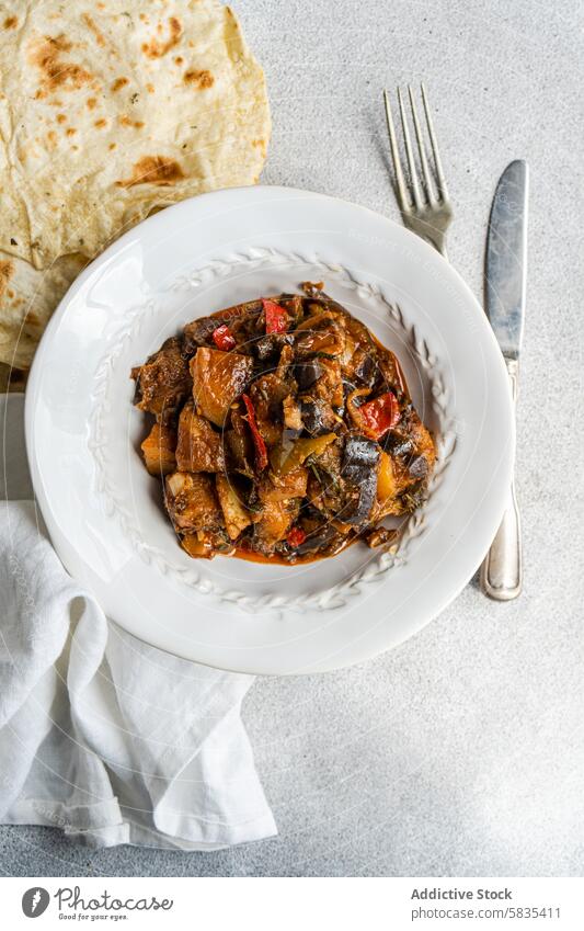 Hausgemachter Gemüseeintopf und Fladenbrot auf einem weißen Teller schmoren Aubergine Tomate Kartoffel Paprika Zwiebel Knoblauch Basilikum selbstgemacht