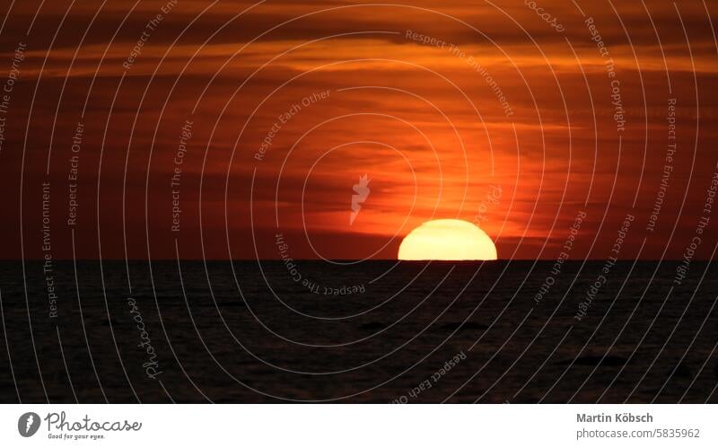 Sonnenuntergang am Horizont der Ostsee. Die orangefarbene Sonne versinkt im Wasser. Romantisch Sonnenstrahlen Sonnenschein Reflexion & Spiegelung wellig Küste