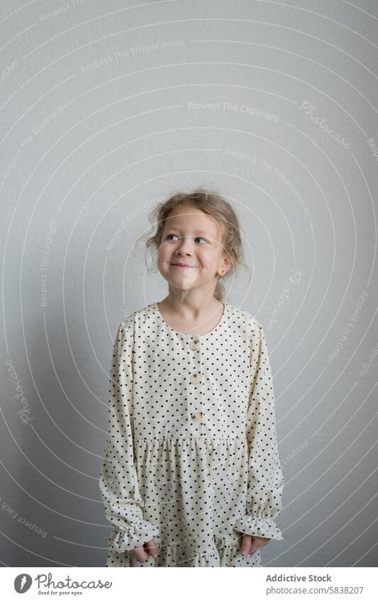 Fröhliches junges Mädchen in einem verspielten Kleid schaut weg Kind Lächeln gepunktet freudig Ausdruck wegschauen Porträt Unschuld heiter Glück niedlich