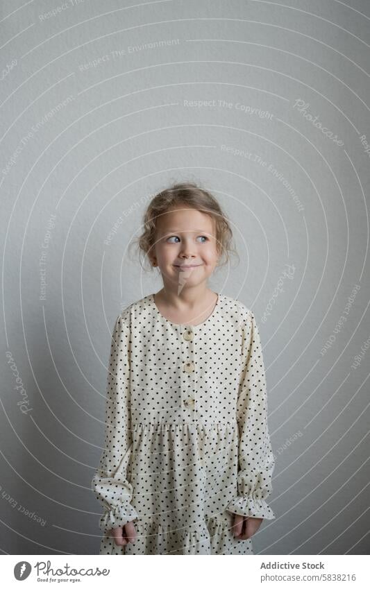 Fröhliches, nach oben blickendes junges Mädchen in einem gepunkteten Kleid Kind Lächeln Punktmuster niedlich Freude Fröhlichkeit Blick aufwärts Ausdruck subtil