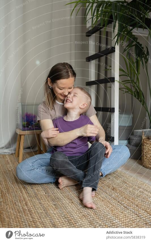 Zärtlicher Moment zwischen Mutter und Kind in einem Haus Sohn Umarmung Lachen heimwärts Familie Wärme binden Teppich Fischbecken im Innenbereich gemütlich Liebe