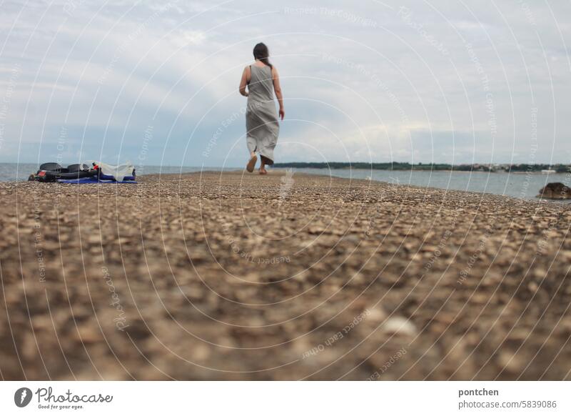 frau geht einen Steg  am Meer entlang. rückansicht meer urlaub steg ferien kleid Fröhlichkeit Kaukasier Leben rücken von hinten schnorchel taucherbrille bewölkt