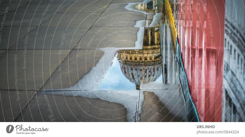 Die Kuppel der Kathedrale (St. Paul’s Cathedral) spiegelt sich in einer kleinen Pfütze auf den Gehwegplatten, direkt neben einer plakatierten Wand Spiegelung