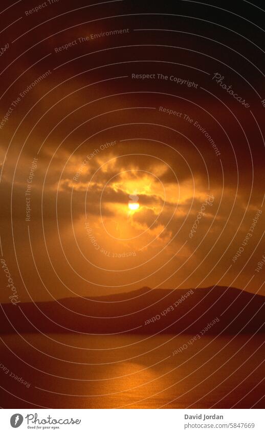 orange-goldener Sonnenuntergang mit dunklen Regenwolken über dem orangenen Mittelmeer mit Insel Sonnenuntergangshimmel Regenwolken über dem Meer mit Insel