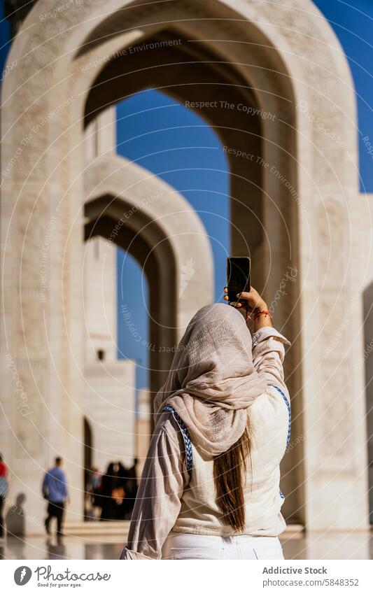 Frau erkundet Oman und hält Erinnerungen an architektonische Stätte fest Smartphone Foto Torbogen Architektur reisen Kultur Reise bescheiden Kleidung