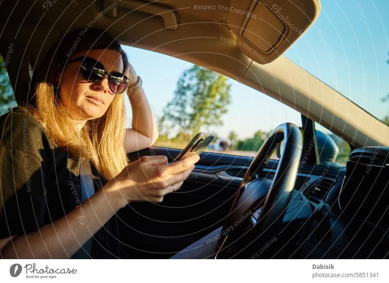 Frau benutzt Smartphone während der Fahrt im Auto PKW fahren Sonnenbrille Fahrer Sicherheit Ablenkung Straße Fahrzeug Nachmittag sonnig Sitz Gerät