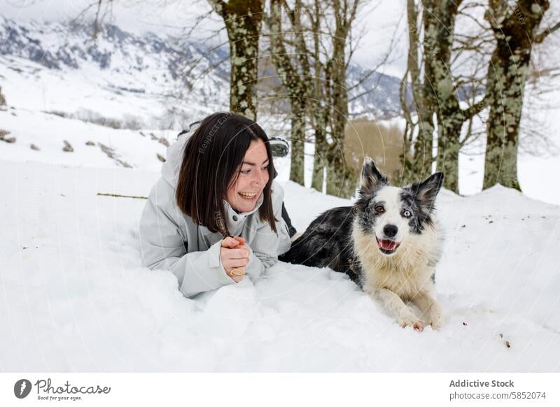 Frau und Border Collie Blue Merle liegend im verschneiten Wald blue merle Schnee Winter Bäume Berge u. Gebirge Lächeln spielerisch Interaktion Lügen Haustier