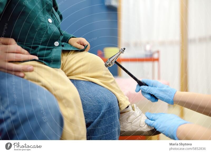 Ein Baby und seine Mutter werden von einem Kinderneurologen in einer modernen medizinischen Klinik untersucht. Der Arzt führt Tests durch, überprüft die Reflexe mit dem neurologischen Hammer des kleinen Patienten. Hochqualifizierte Heilung