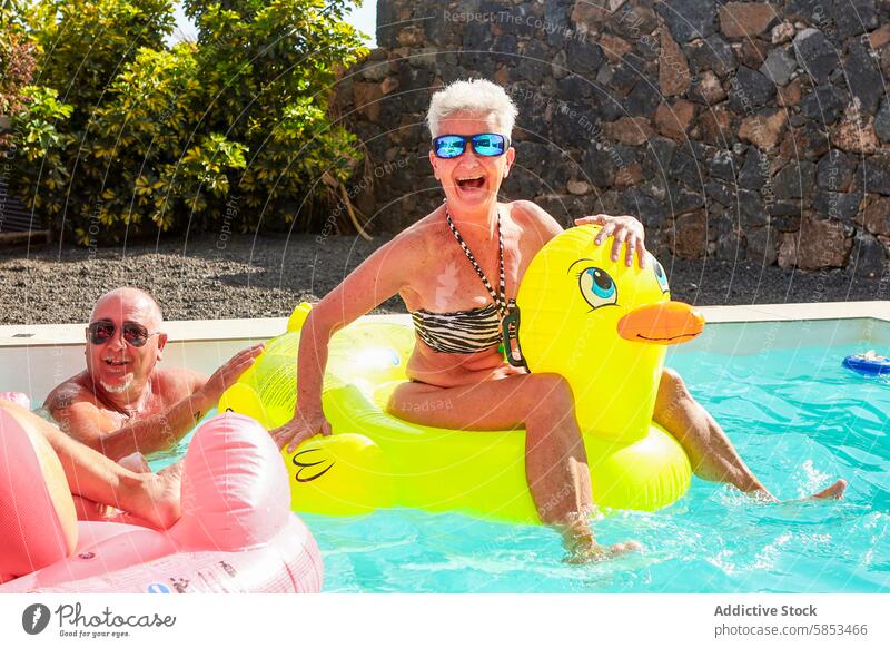 Fröhliche Senioren, die einen sonnigen Tag im Schwimmbad genießen aufblasbar Spielzeug Ente Schwimmer Paar Wasser Spaß Freude Sommer im Freien Freizeit