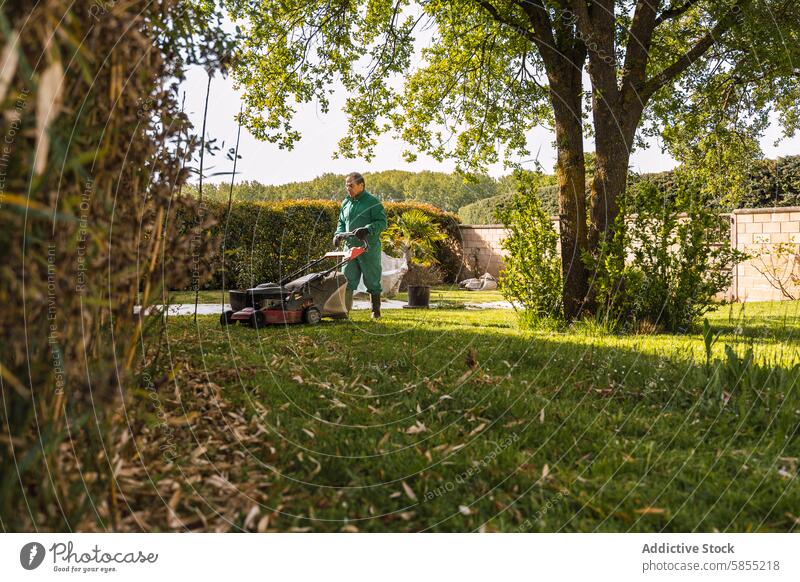 Mann mäht einen üppigen grünen Rasen in einem ruhigen Garten Mähen Uniform Rasenmäher Gelassenheit Bäume Pflanzen im Freien Aktivität Gartenarbeit