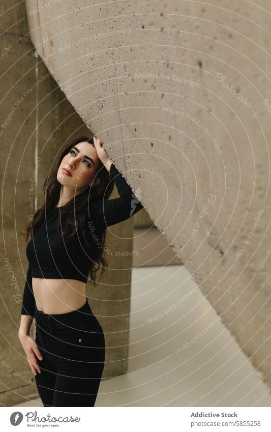 Junge Frau in städtischer Umgebung, die nachdenklich posiert jung urban Beton Pose Behaarung Blick Stehen Wand schwarz lässig Mode ernst Schönheit Model