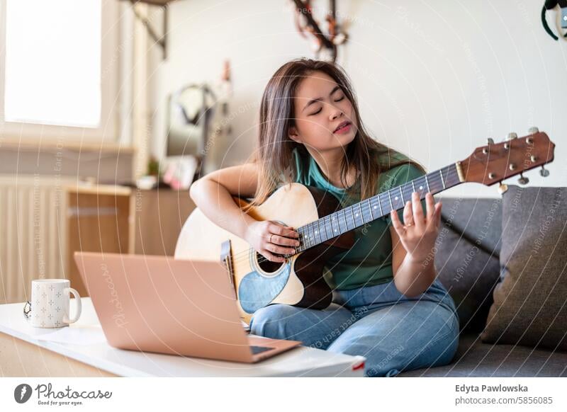 Junge Frau spielt Gitarre zu Hause asiatisch echte Menschen Spaß genießend junger Erwachsener authentisch heiter selbstbewusst Glück Freude Jahrtausende